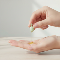 Hand pouring a small amount of liquid from a dropper into another hand on a neutral background